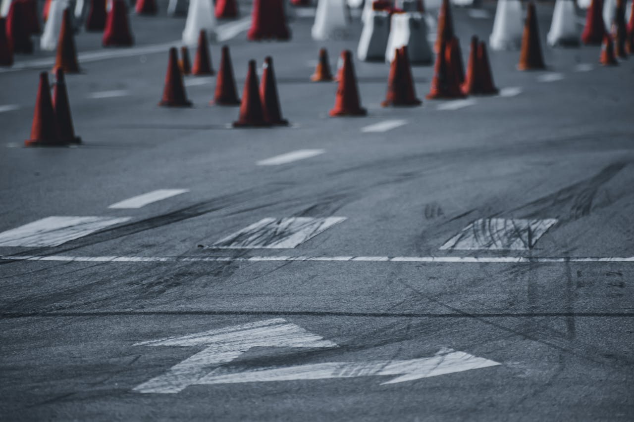 Asphalt roadway with black wheel tracks and red road cones placed on city street in daytime