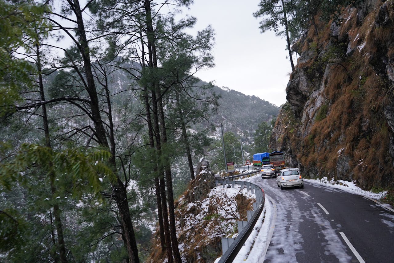 A scenic winter drive on a winding snow-covered road in a forested mountain region, featuring vehicles.